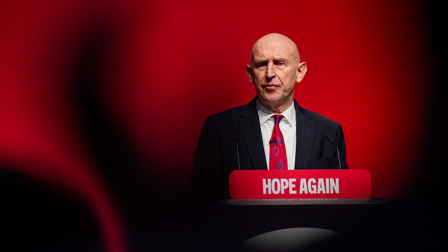 John Healey stands at a podium reading “Hope Again” while speaking at the Labour Party Conference.