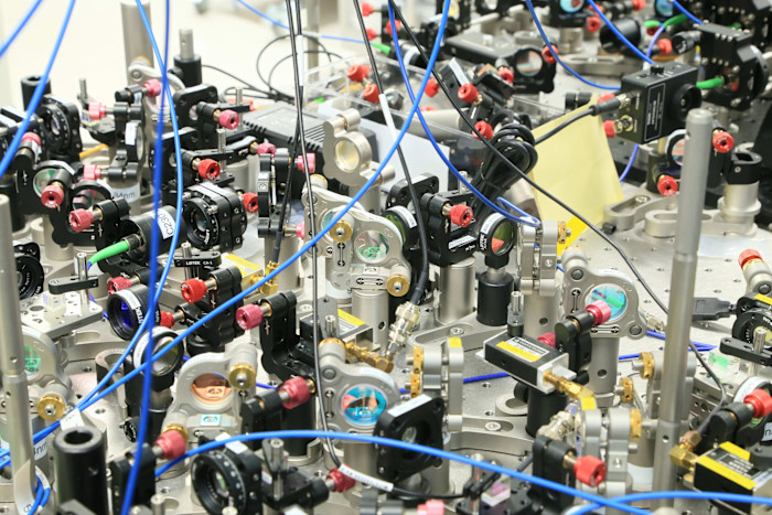 An optical set-up with mirrors, lenses and cables arranged on a metal table, used for a nuclear clock experiment.