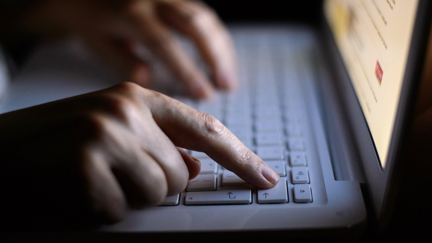 Hands typing on a laptop keyboard, with the screen partially visible and out of focus.