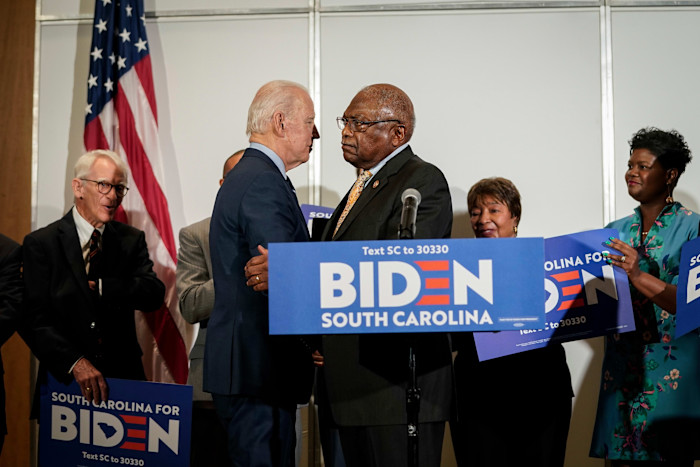 Joe Biden shakes hands with Jim Clyburn as they stand at a podium with “Biden South Carolina” signs during an endorsement event.