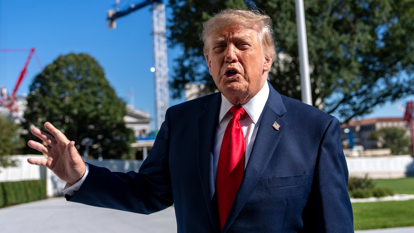 Donald Trump gestures while speaking to reporters outdoors on the White House grounds, with construction cranes visible in the background.