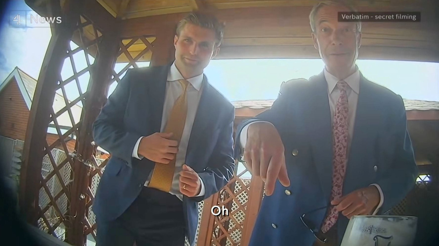 Nigel Farage (right) and Dan Jukes (left) in suits inside a wooden gazebo, filmed by a hidden camera.