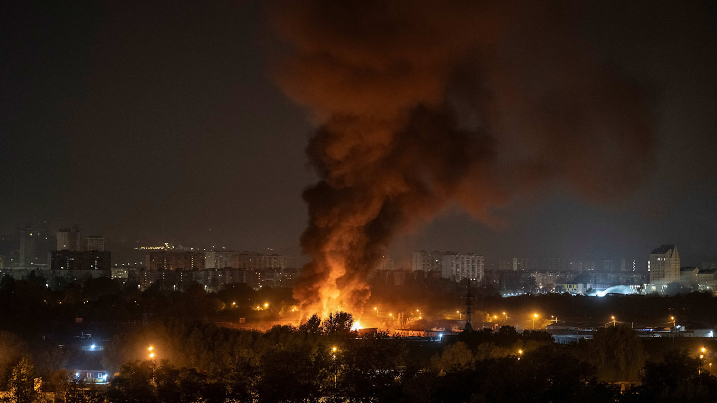 Thick black smoke and flames rise from a fire in Kyiv at night, with city buildings visible in the background.