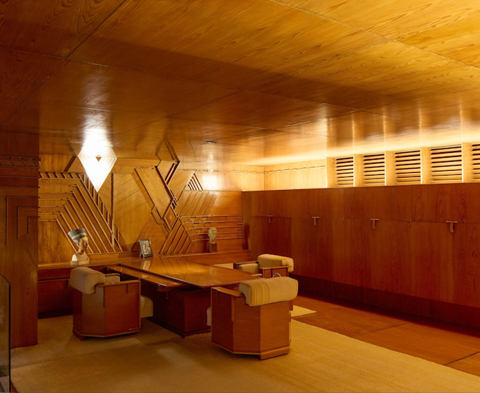 Frank Lloyd Wright’s Kaufmann Office features geometric wooden panelling, built-in cabinetry, a large wooden desk and upholstered chairs.