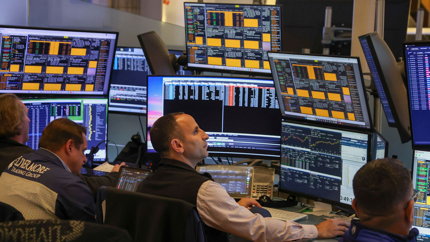 Traders at desks monitor multiple screens displaying financial data on the floor of the New York Stock Exchange before the closing bell.