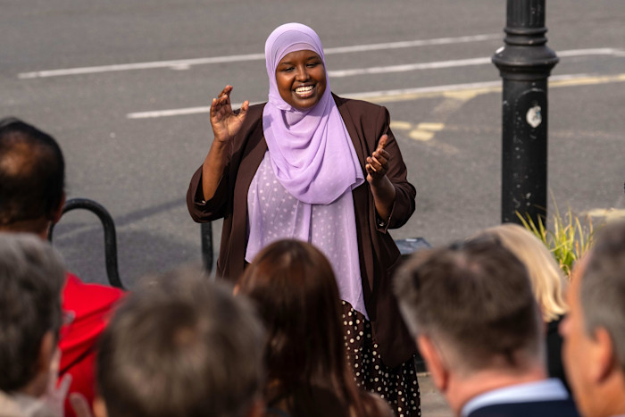 Sagal Abdi-Wali speaks to a group of activists and supporters outdoors, gesturing with her hands and smiling.