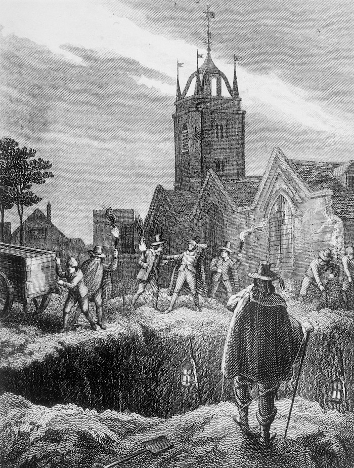A group of men with torches prepare to empty a covered cart into an open mass grave at night in a churchyard during the London Plague of 1665.