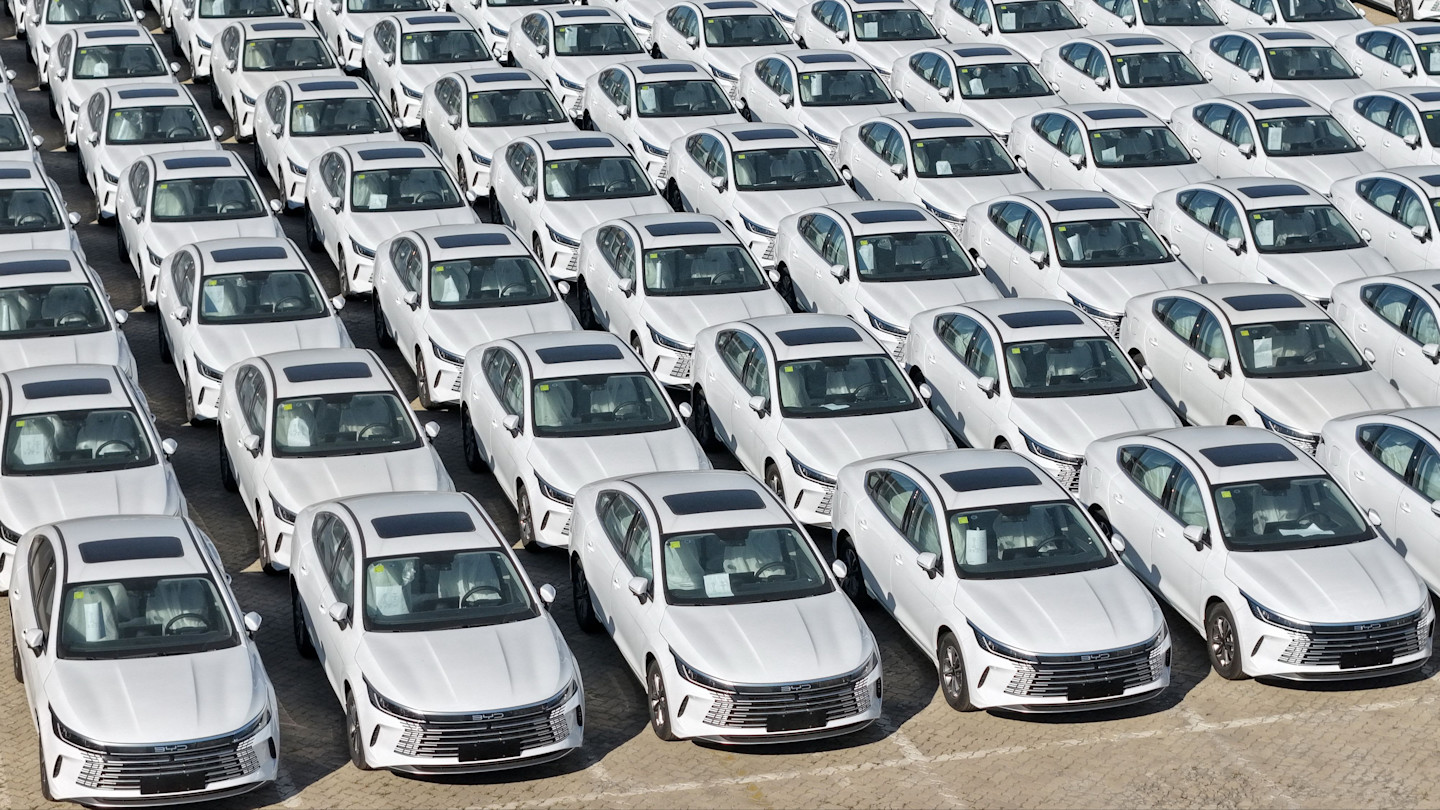 Rows of new white BYD hybrid cars parked closely together, viewed from above, awaiting shipment to dealerships.