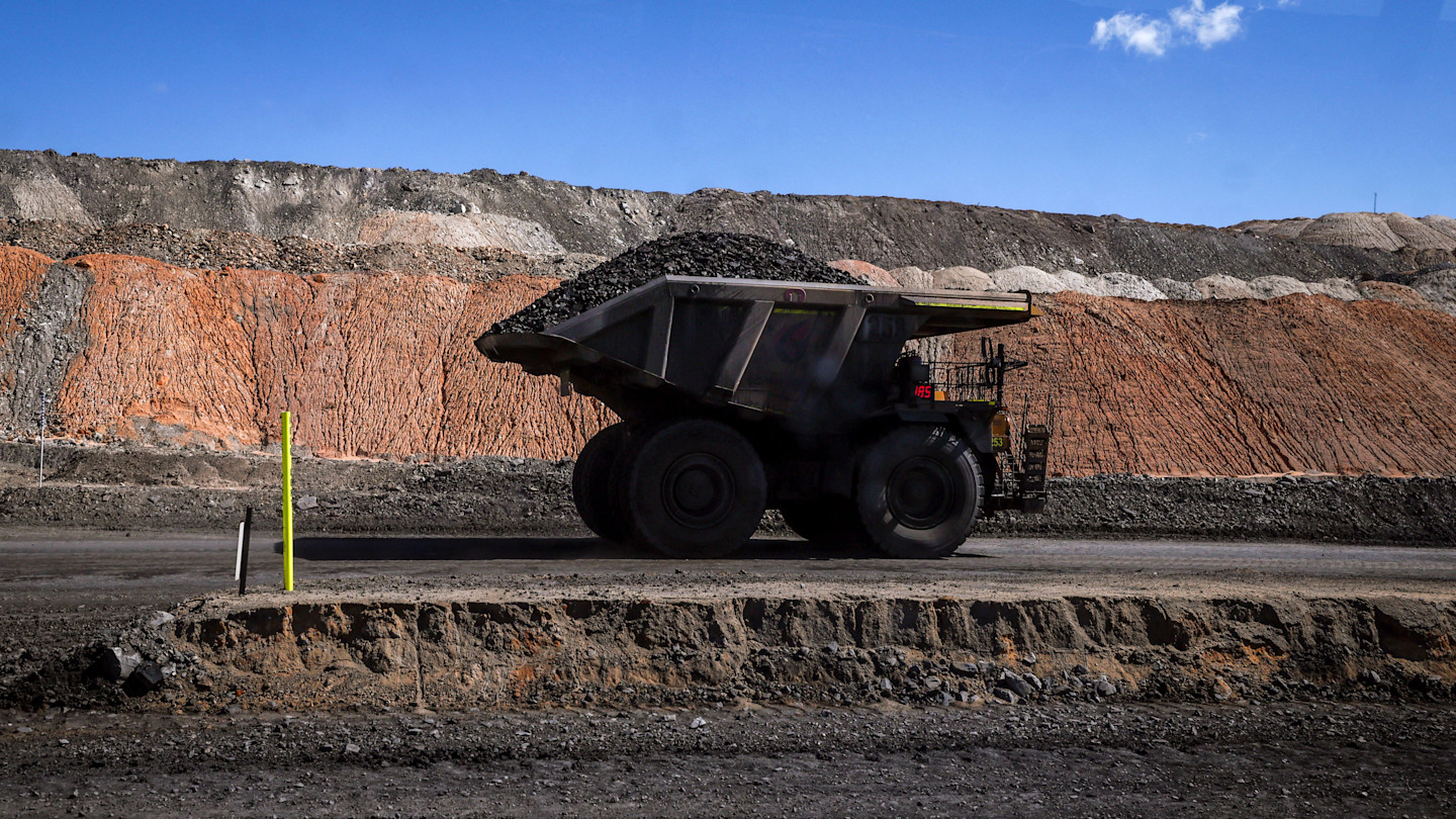 A coal hauler truck loaded with coal drives on a road at the Moolarben coal mine, with exposed layers of earth in the background.