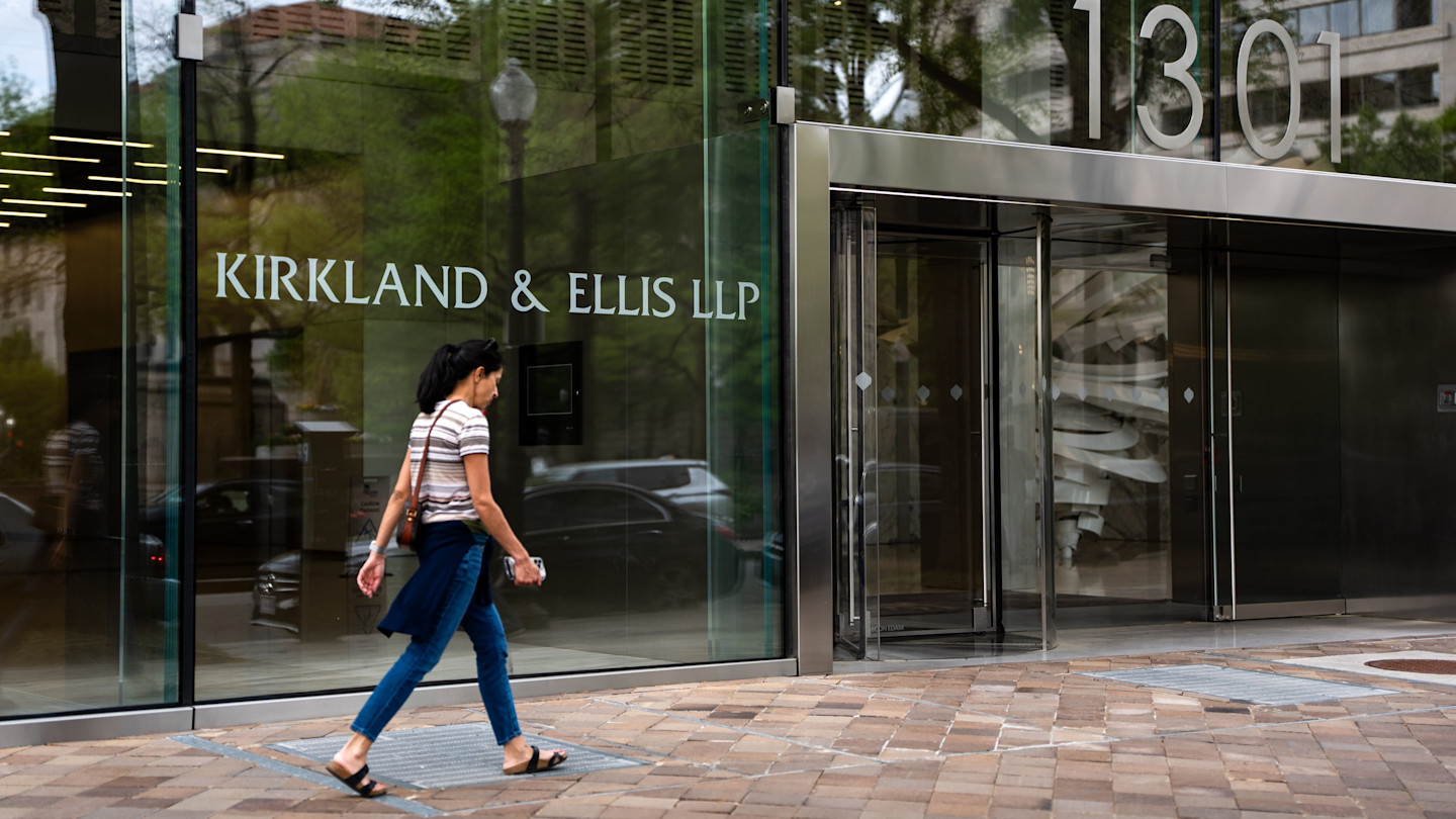 A woman walks past the entrance of the Kirkland & Ellis LLP law firm, with the firm's name and building number 1301 visible on the glass facade.