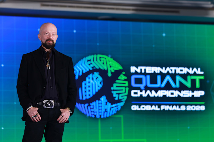 Igor Tulchinsky stands in front of a screen displaying the International Quant Championship Global Finals 2026 logo.