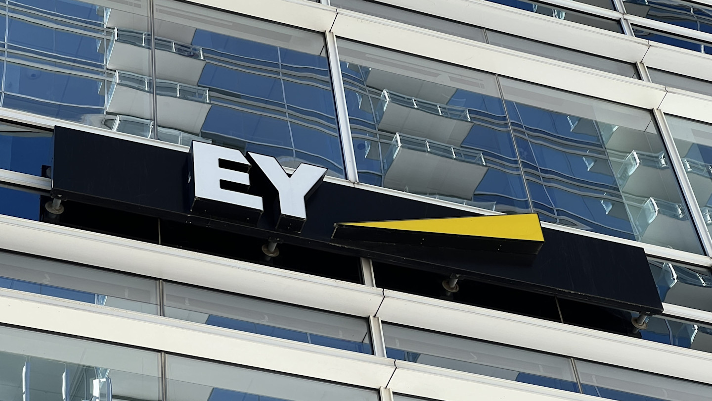 Sign for Ernst & Young (EY) with white letters and a yellow accent on the exterior of a glass office building.