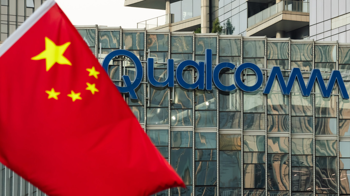 A Chinese national flag in front of a Qualcomm logo on the glass facade of an office building.