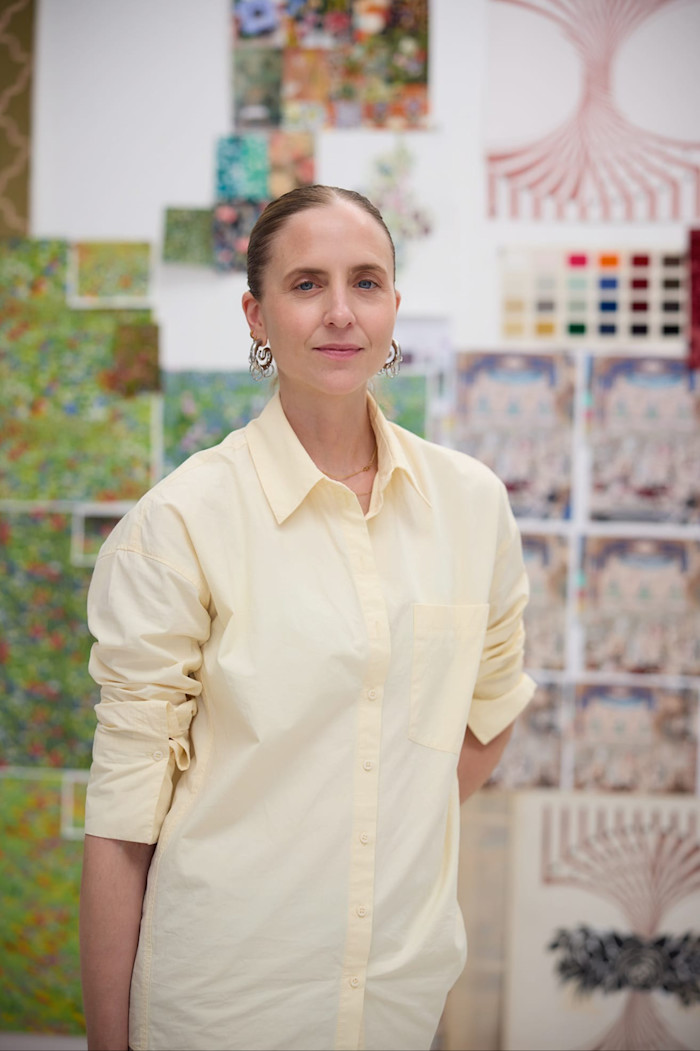Yelena Ford stands in front of a wall covered with colourful art prints and pattern samples.