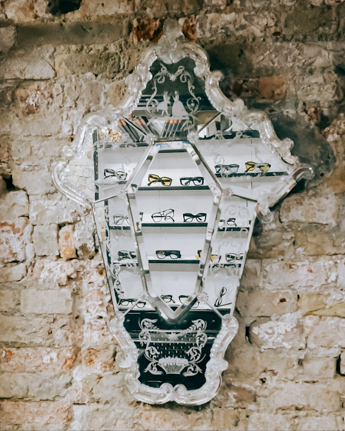 A display of glasses reflected in an ornate mirror on a bare brick wall.