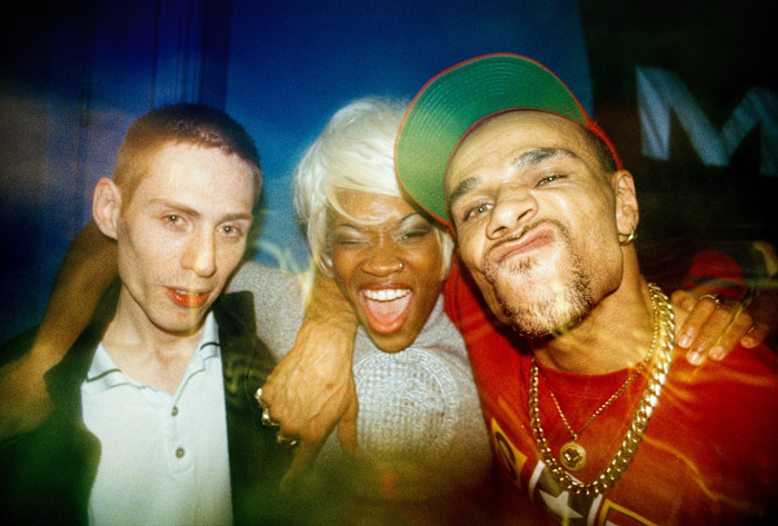 Three people at a club, smiling and posing closely together; one is making a playful face, another is winking and laughing.