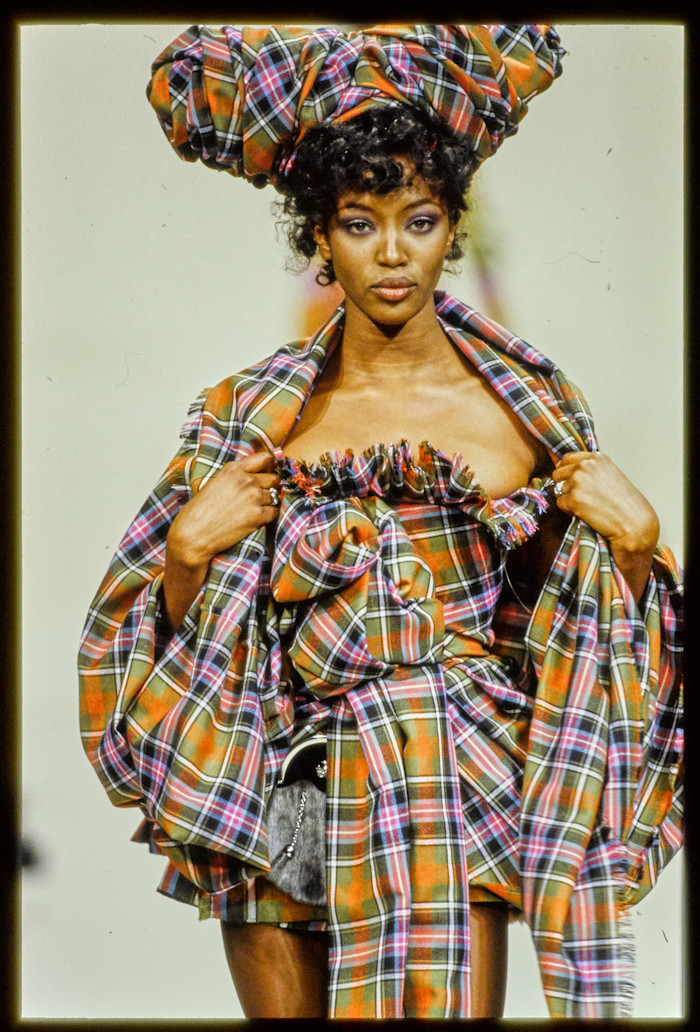 Naomi Campbell models a voluminous tartan ensemble with a large matching headpiece on the Vivienne Westwood Fall 1994 runway.