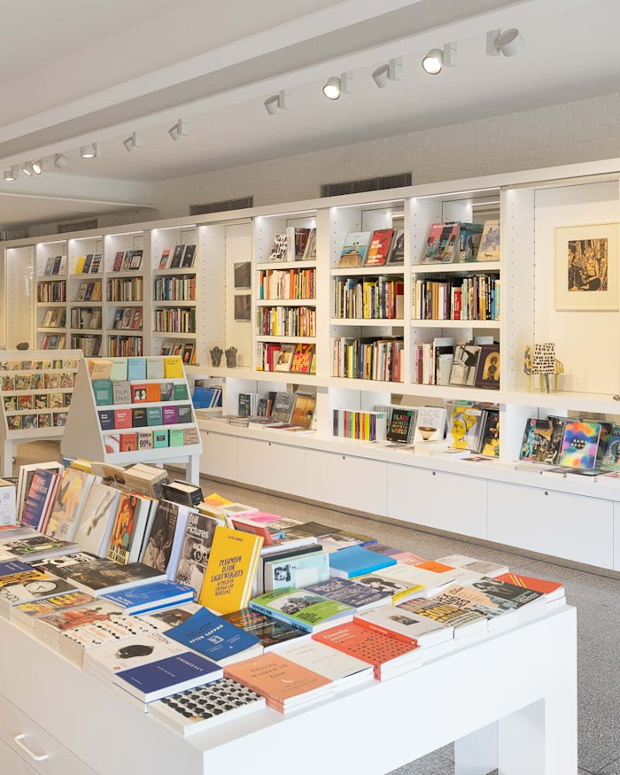 Bright, modern bookshop interior with white shelves and tables displaying art books, magazines, and postcards at Camden Art Centre Shop.