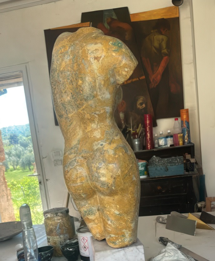 Sculpture of a headless female torso displayed on a plinth in an artist’s studio.