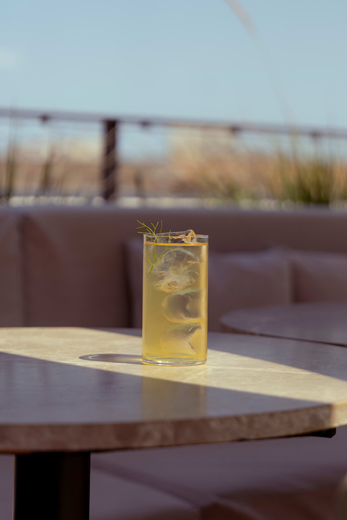 An iced cocktail with a sprig of leaf on an outside terrace table.