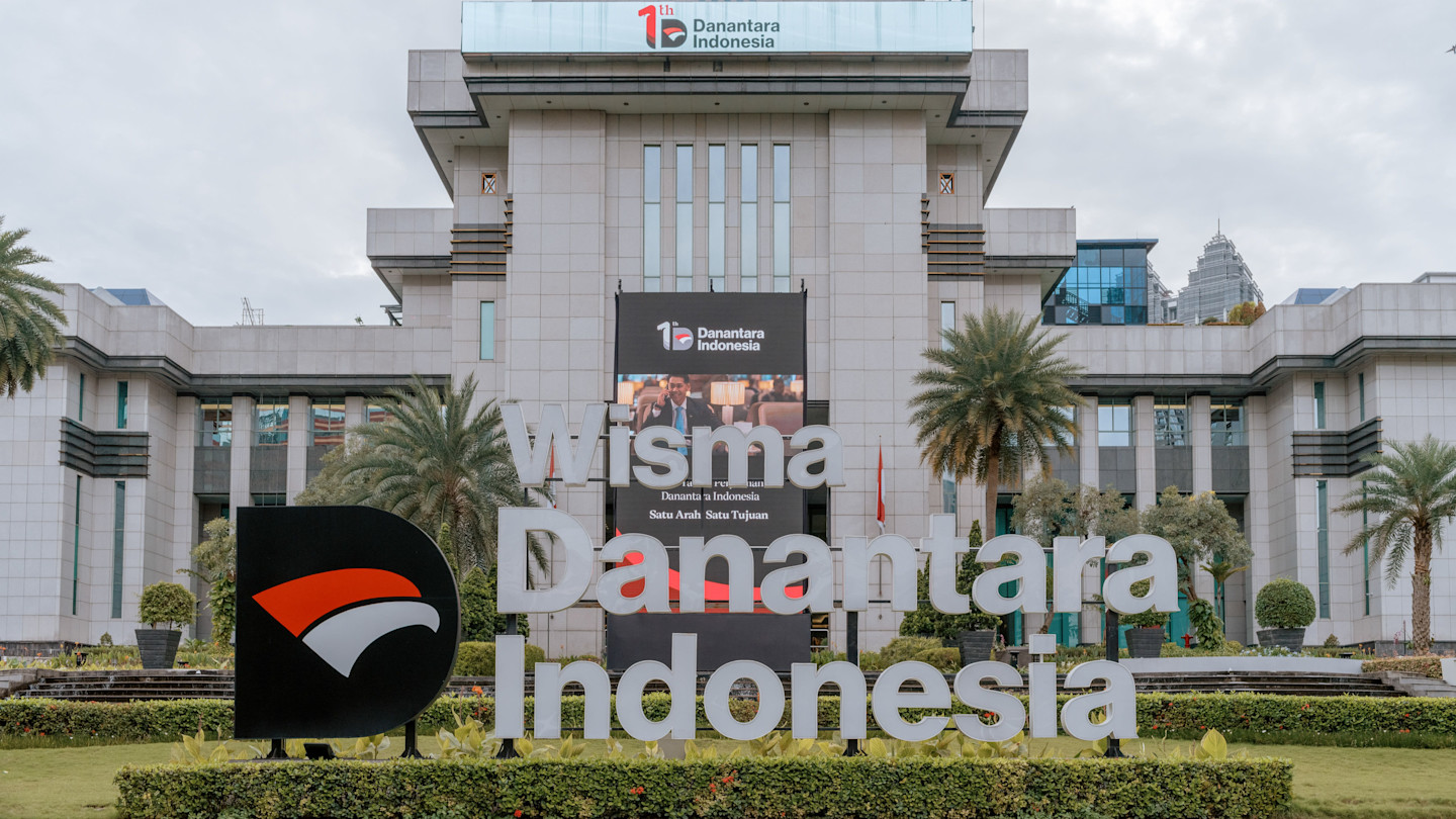 The Danantara HQ in Jakarta building with a large sign and palm trees in front.