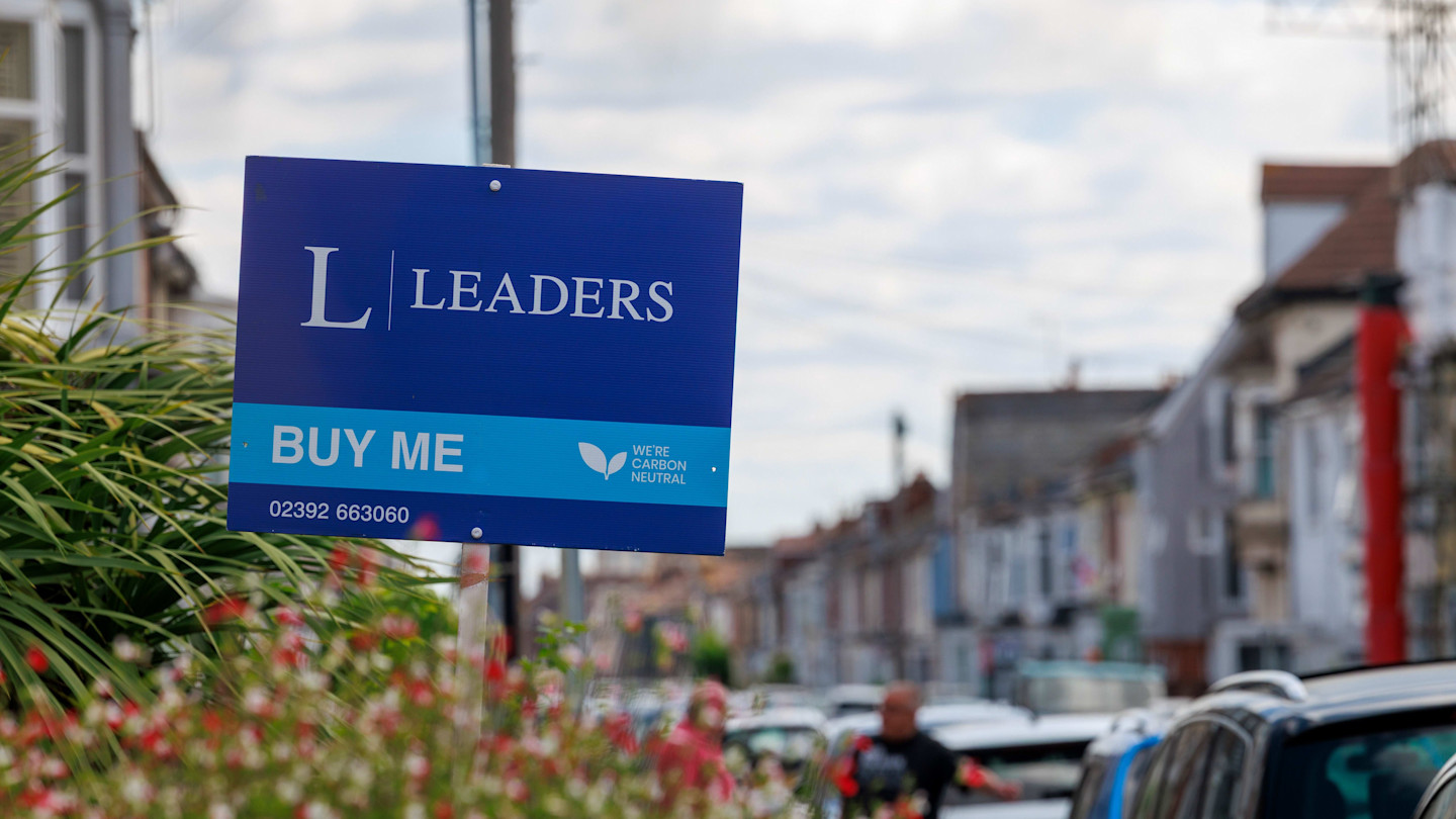 A Leaders estate agent sign reading ‘Buy Me’ outside a row of residential houses in Portsmouth, UK.