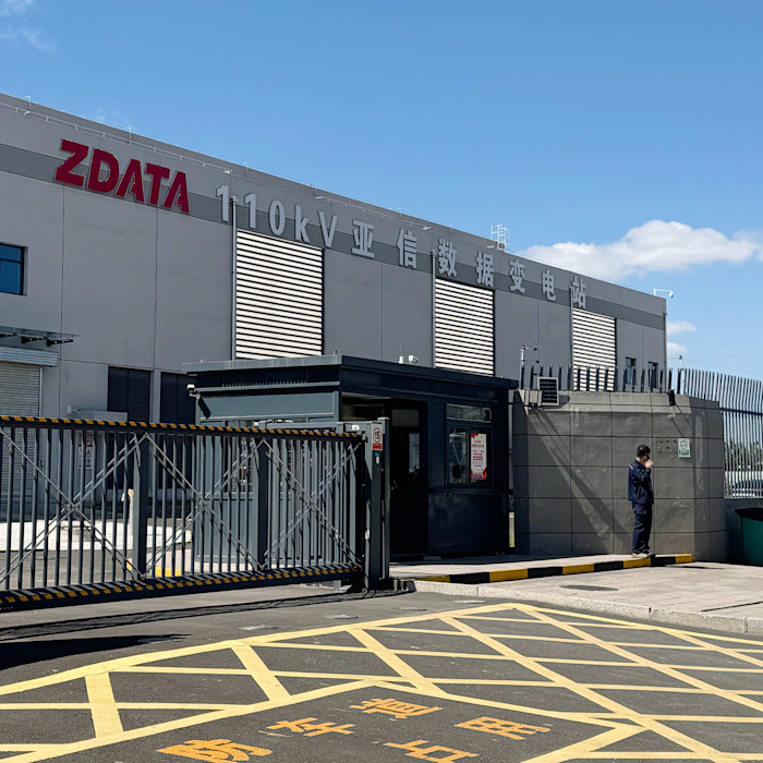 A data centre building with ‘ZData’ signage and a fenced entrance. A person stands near the gate outside.