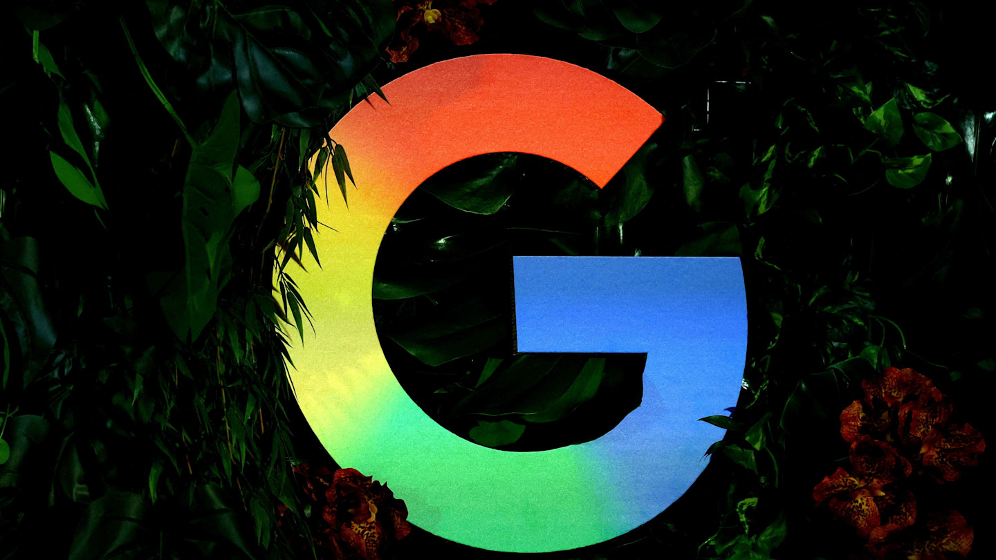 The Google logo in rainbow colors against a background of green leaves and red flowers