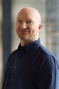 Russell Davies, head of legal and compliance operations at Dentsu, smiling and standing in a dark shirt.