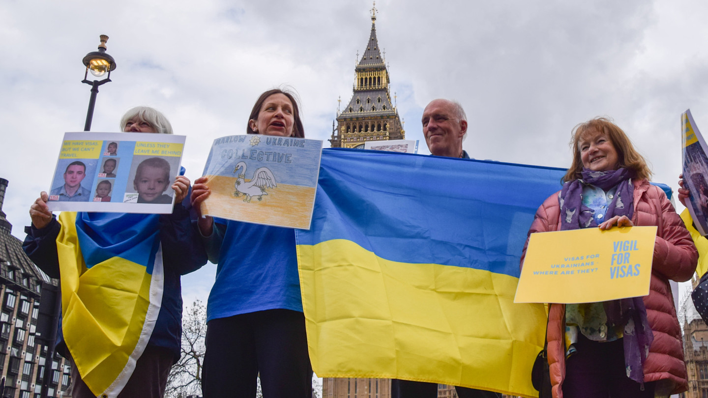 Protesters in parliament square hold a Ukrainian flag and signs supporting faster visa processing for Ukrainian refugees.
