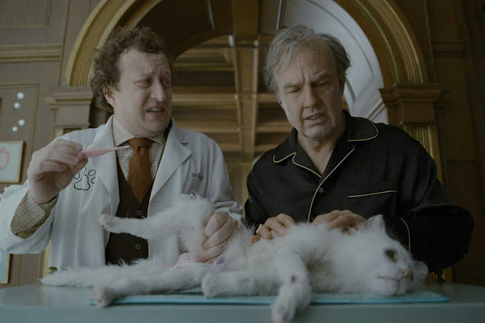 Ross Hatt as Dr Berg and Tom Cruise as Rockwell stand over Maggie The Cat, who is lying on an exam table.