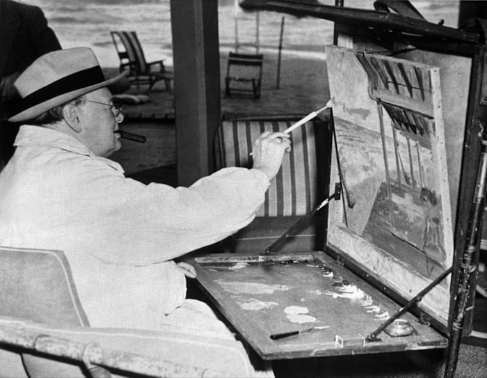 Winston Churchill painting a seaside scene at an easel, seated with a cigar in his mouth at the Surf Club in Miami.