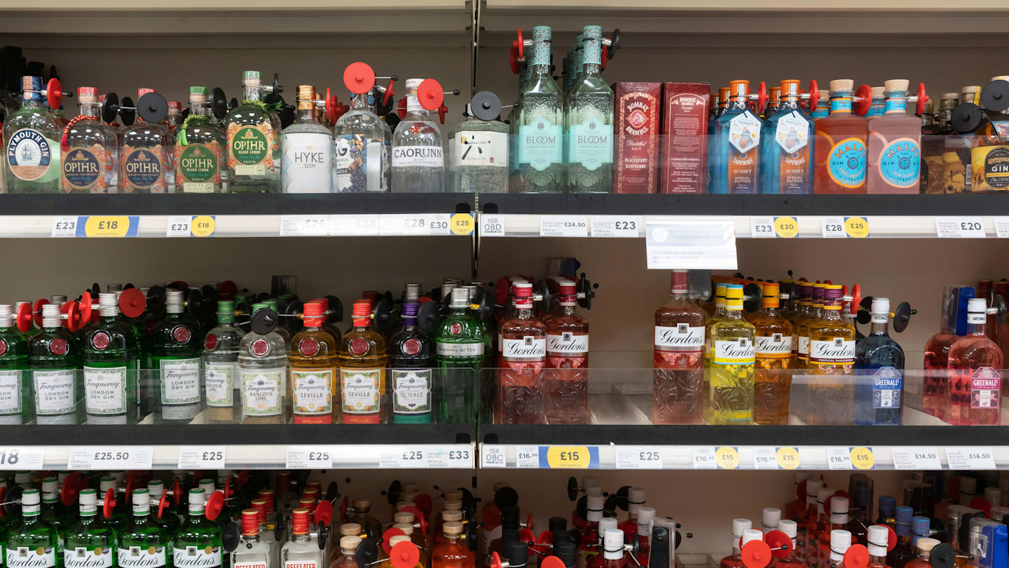 Several brands of gin, each bottle fitted with a red security tag, are displayed on Tesco supermarket shelves.