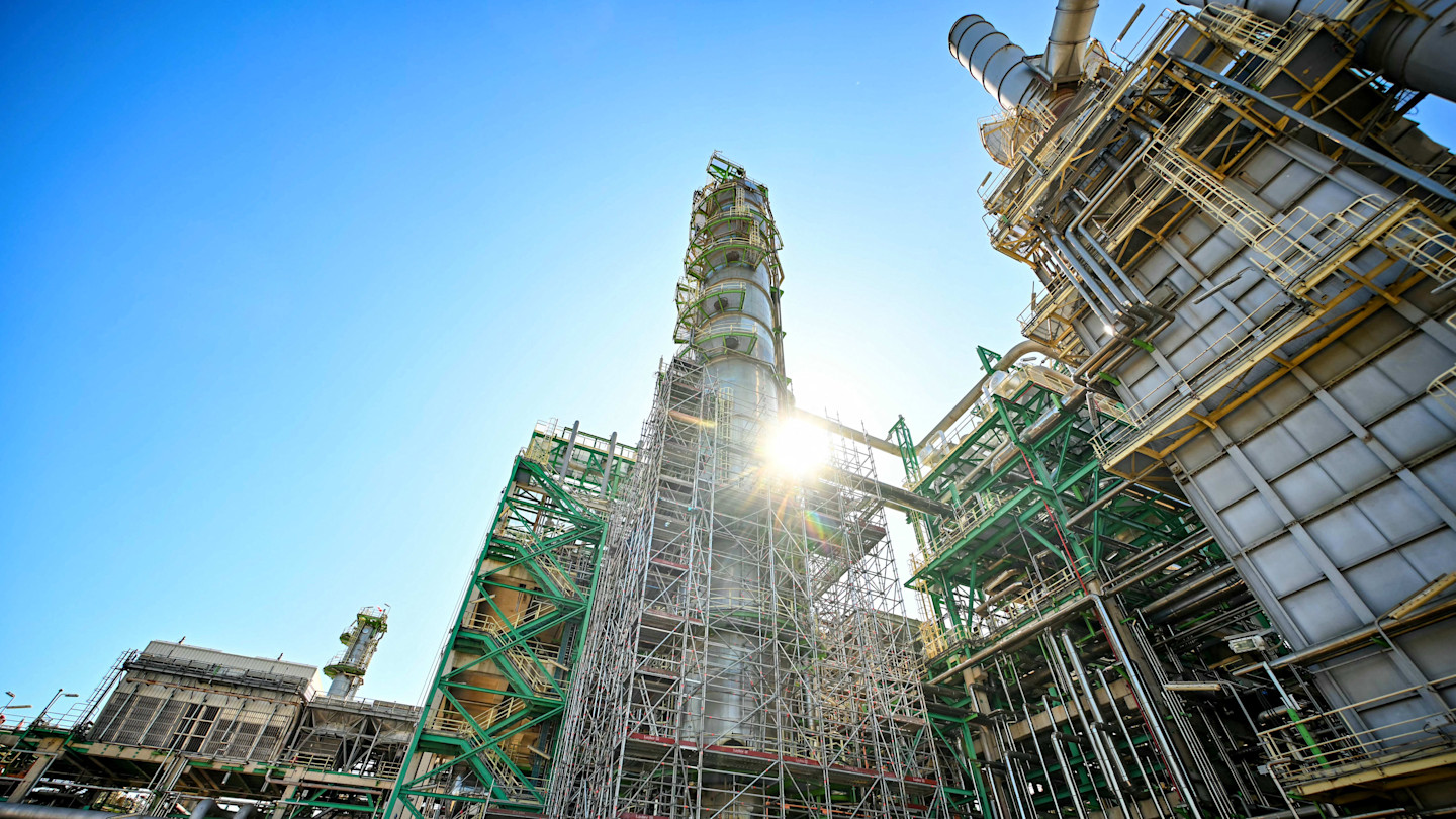 TotalEnergies refinery platform with scaffolding and industrial structures under a clear blue sky, sunlight shining through.