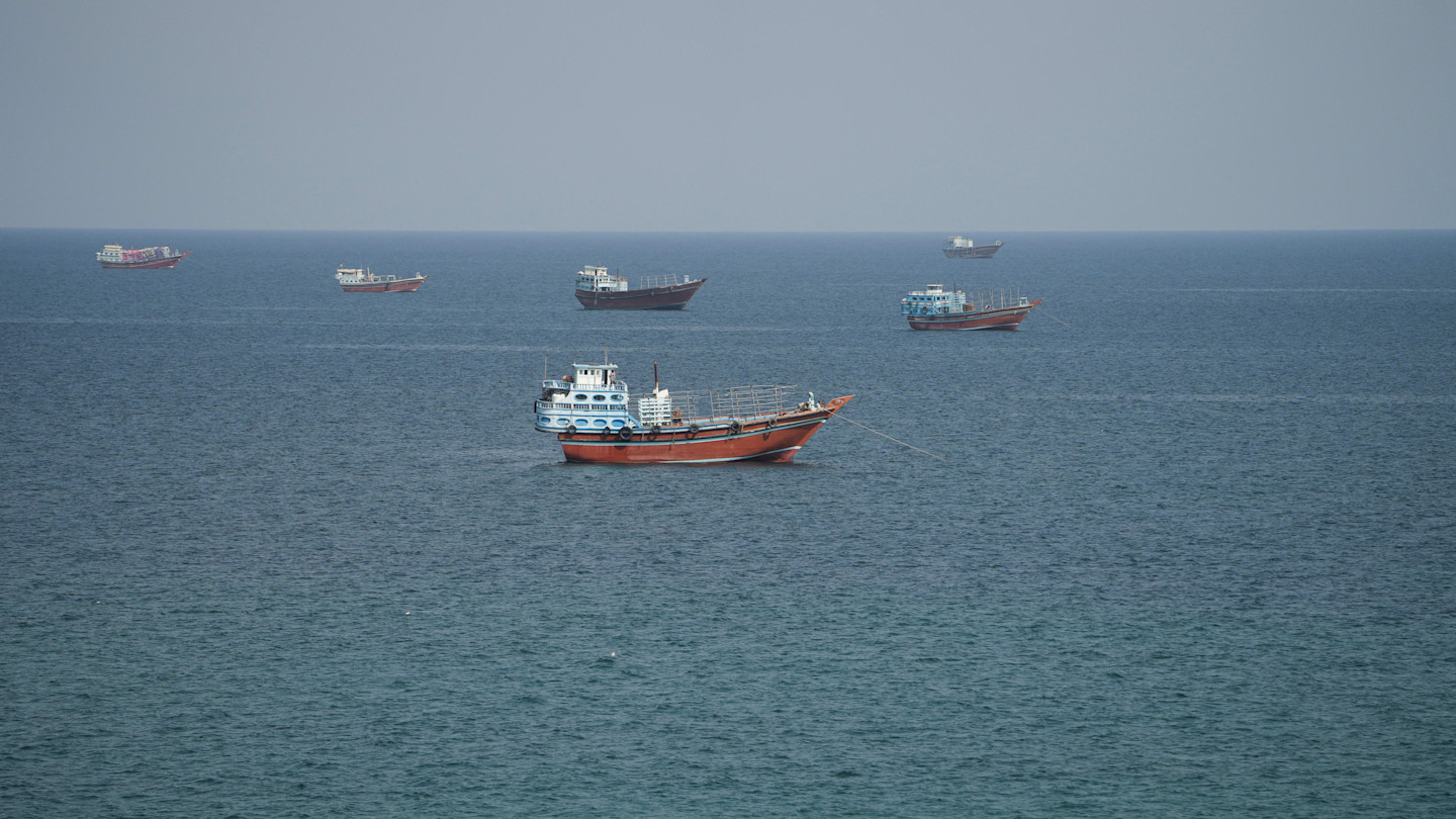Several fishing and cargo vessels are scattered across calm blue waters in the Strait of Hormuz.