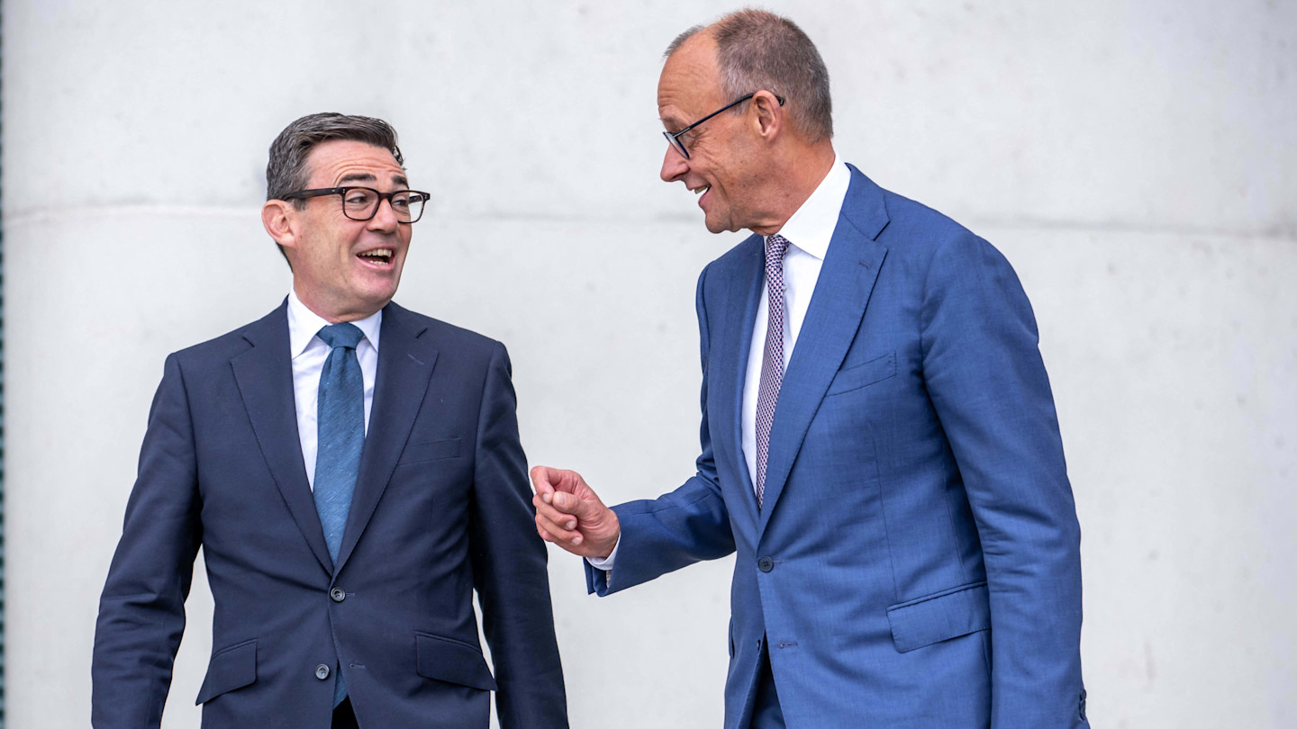 Friedrich Merz, right, speaks with Andy Burnham as they walk together, both wearing suits and appearing engaged in conversation.