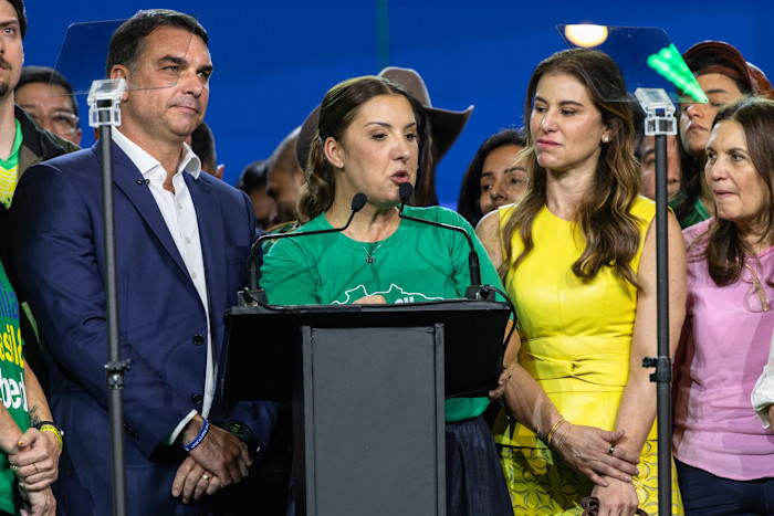 Daniella Marques speaks at a podium between Flávio Bolsonaro and two women during a campaign launch event in São Paulo.