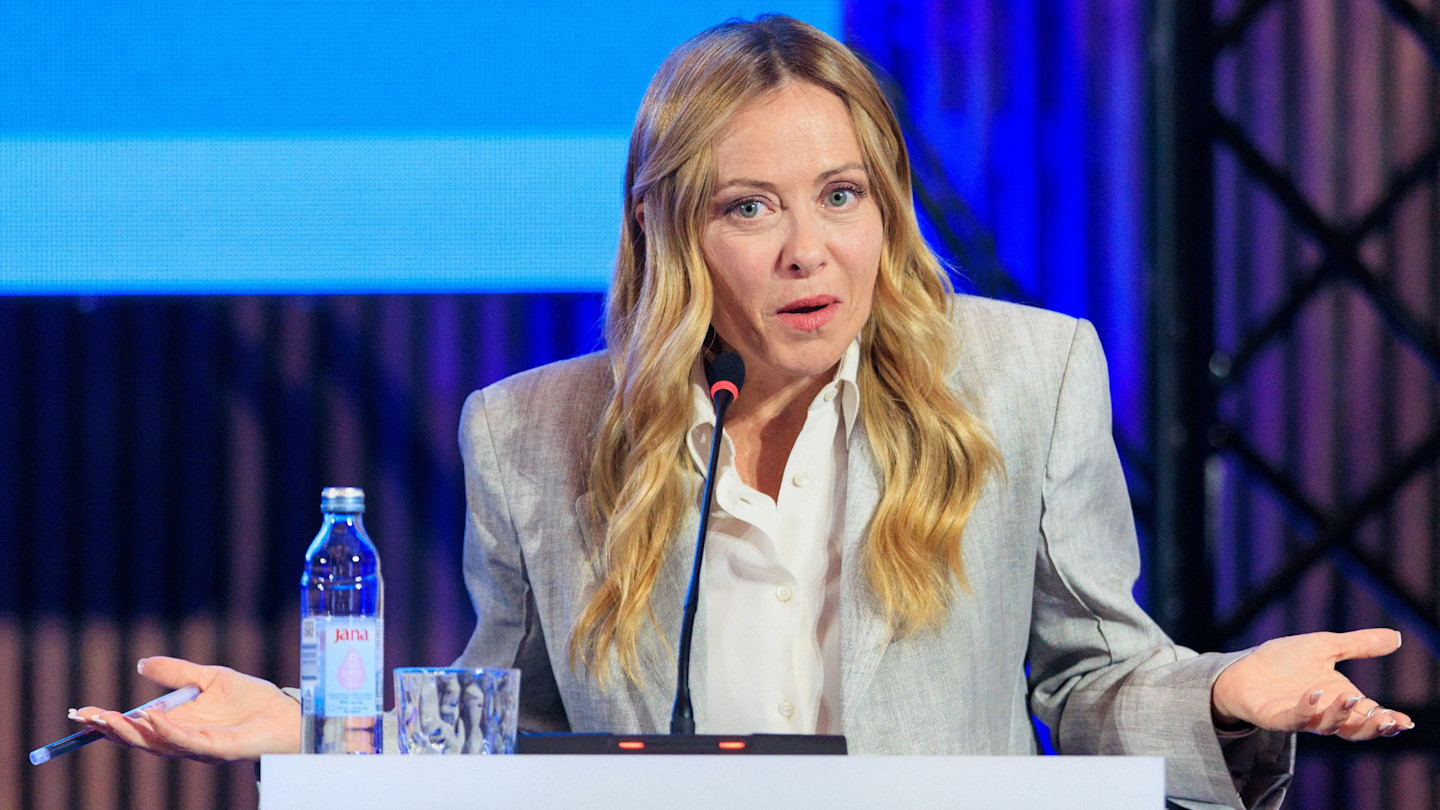 Giorgia Meloni speaks at a podium with a microphone, gesturing with her hands.