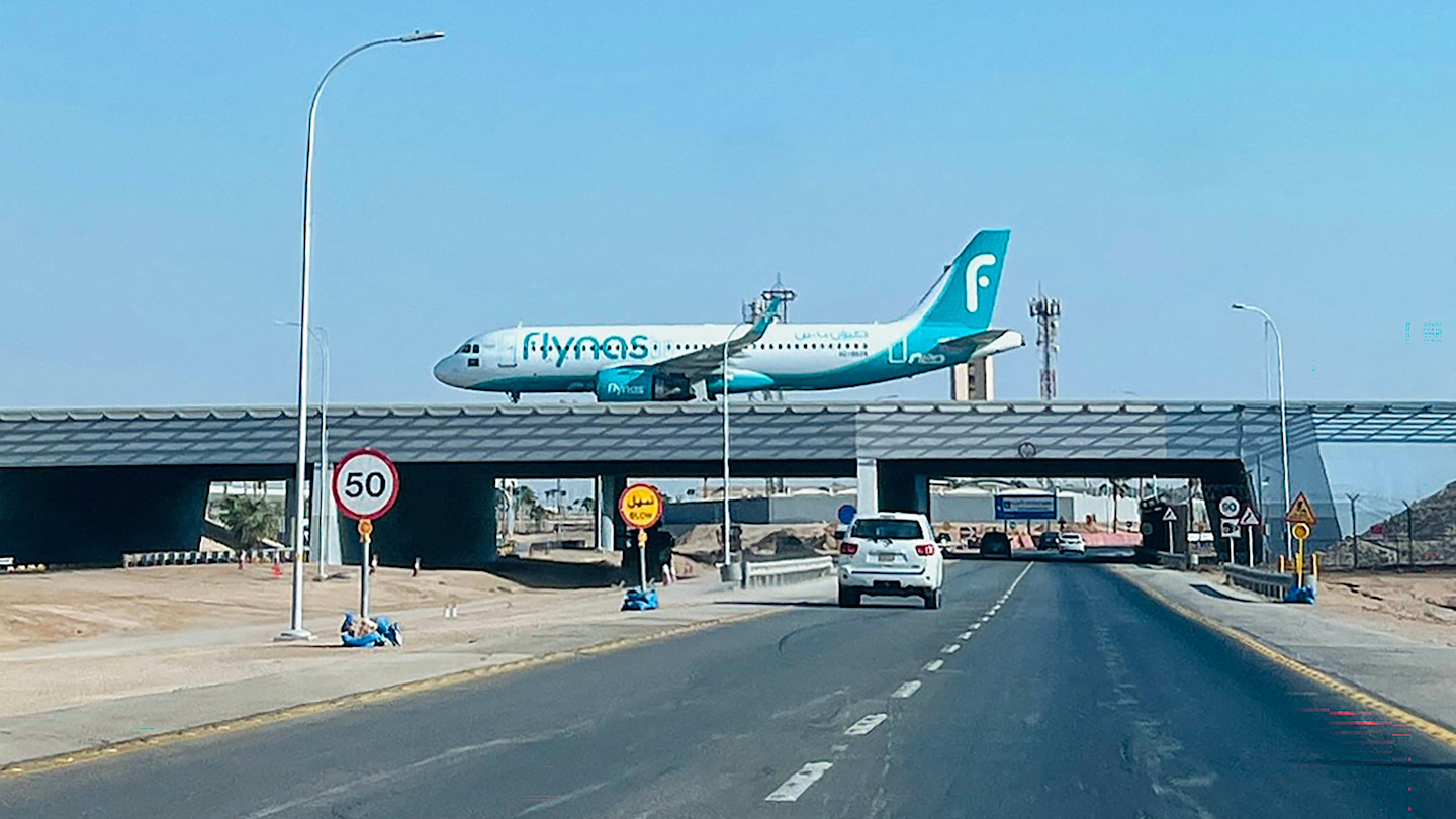An aeroplane prepares to land, taxiing above a road near King Khalid International Airport as cars drive below.