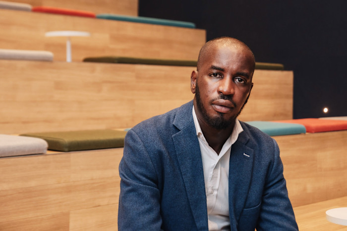Nana Agyemang seated in a blue blazer and white shirt, looking at the camera.