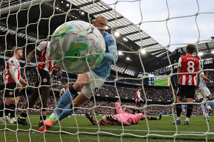 Erling Haaland turns to celebrate after scoring a goal for Manchester City against Brentford, with the ball in the net and Brentford players reacting.