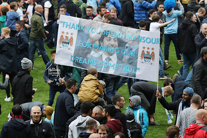 Manchester City fans on the pitch hold a banner reading, “Thank you Sheikh Mansour for making our dreams come true.”