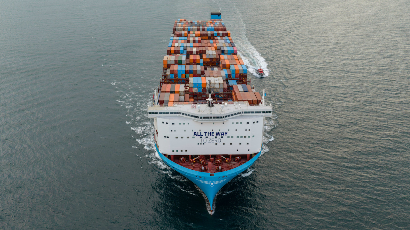 A Maersk container ship with “All the way to zero” written on the bow sails off the coast, stacked with multicoloured containers.