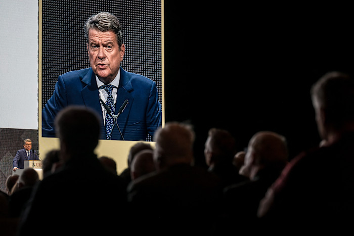 Colm Kelleher speaks at a podium, shown on a large screen, as attendees watch during the UBS annual general meeting.