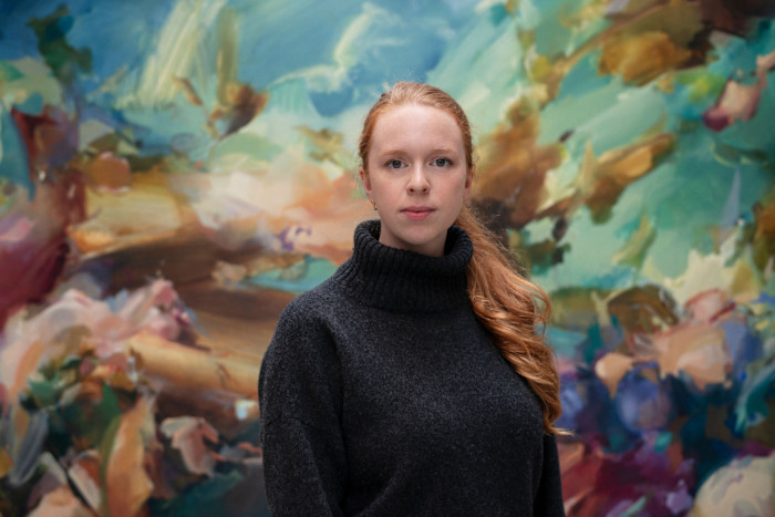 Flora Yukhnovich stands in front of a large, colorful abstract painting in her studio.