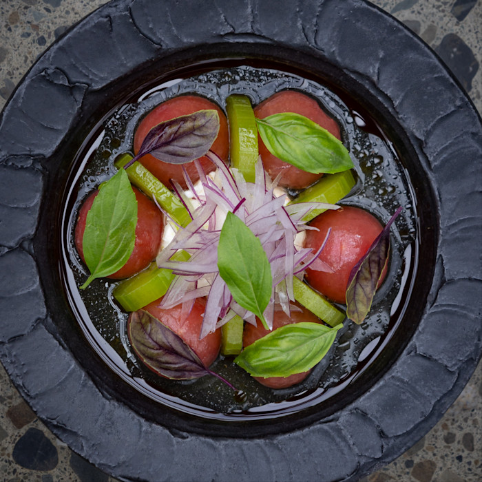 A salad arranged with peeled tomato pieces, sliced green peppers, thinly sliced red onion, and fresh basil leaves in a dark bowl.