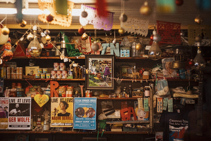 Wooden shelving crammed with groceries and bric-a-brac, with posters advertising ‘Live at Levis’ hanging from the front of shelves.