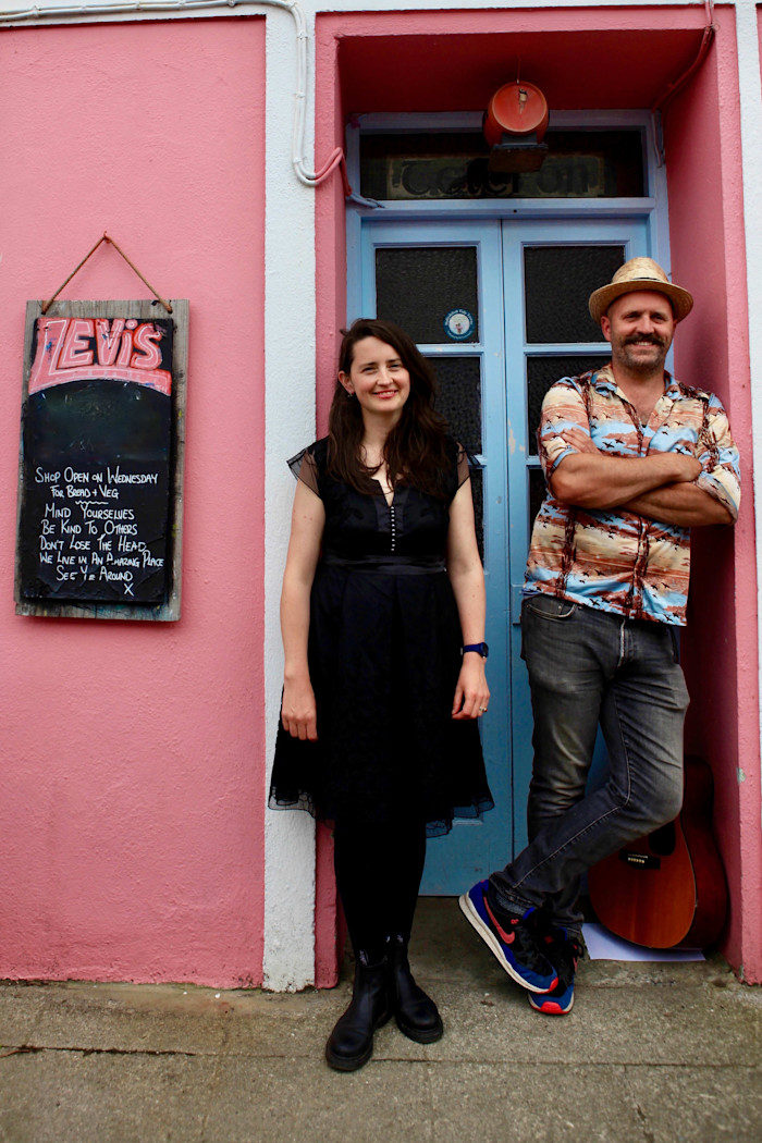 Caroline O Donnell and Joe O Leary standing outside Levis Corner House, with a chalkboard sign and a guitar nearby.