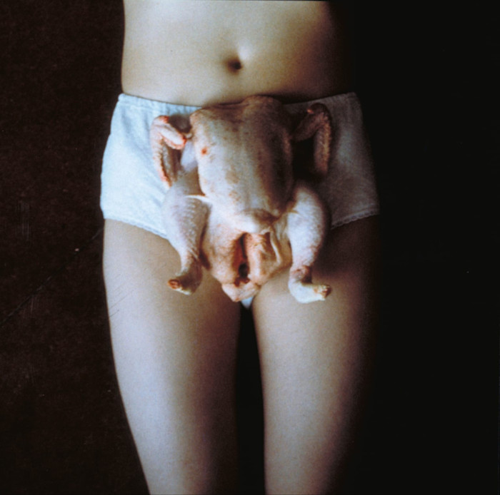 A person stands in white underwear with a raw plucked chicken placed over their groin.