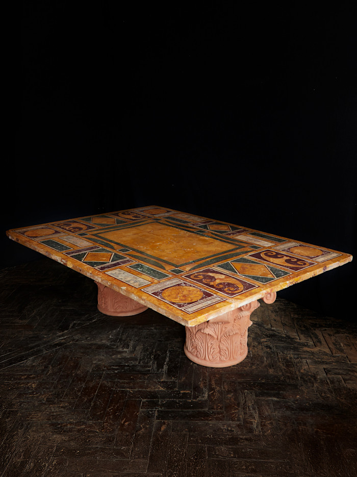 Ornate rectangular table with a multicoloured geometric stone top supported by carved terracotta pedestal bases.